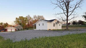 A single-story house with a garage, a gravel driveway, and a grassy yard. - Perfect 2-bedroom house with AC in peaceful Jamestown w/ RV pad (Jamestown)