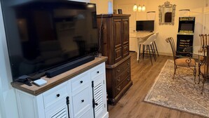 A modern living room with a flat-screen TV, a wooden cabinet, a dining area with a table and chairs, and a patterned rug. - Perfect 2-bedroom house with AC in peaceful Jamestown w/ RV pad (Jamestown)