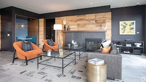 Una sala de estar moderna con chimenea, sofás naranja y grises, una mesa de centro de vidrio y una pared de acento de madera.