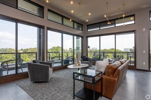 A spacious living area with large windows, a sofa, a coffee table, and a dining table. - Landing | Modern 1BD in Discovery District (Columbus)