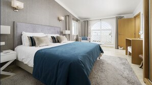 A modern hotel room with a large bed, bedside tables, a desk, and a view of the outdoors. - Casa Descoberta - Luxurious 4 Bedroom family Villa with heated pool (Carvoeiro)