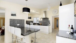 A modern kitchen with granite countertops, white cabinetry, and a central island with bar stools. - Casa Descoberta - Luxurious 4 Bedroom family Villa with heated pool (Carvoeiro)