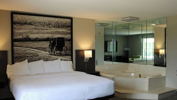 Une chambre d’hôtel moderne dotée d’un grand lit, d’une baignoire, d’un grand miroir et d’une œuvre d’art accrochée au mur.
