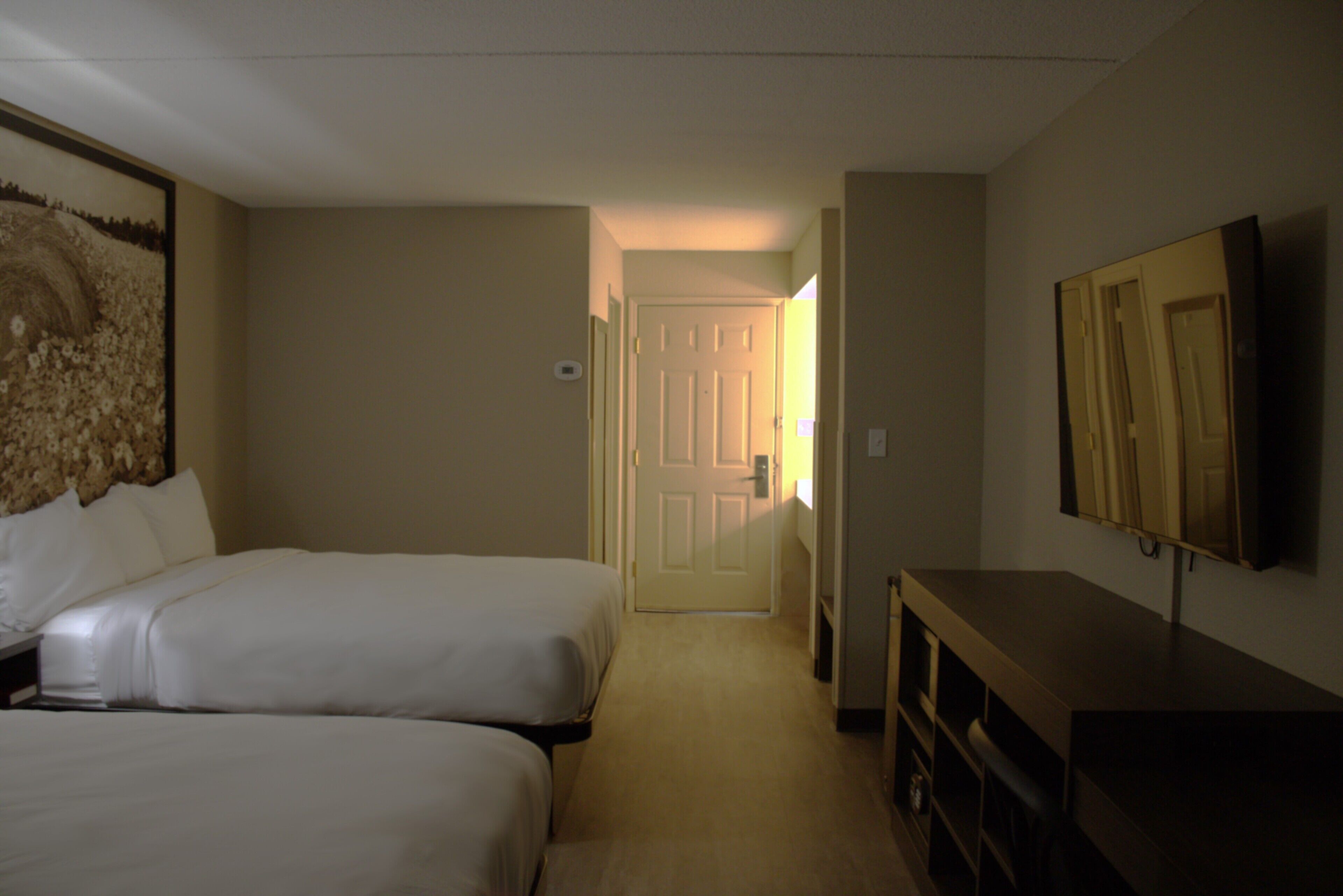 A hotel room with two beds, a TV, and a door leading to another room.