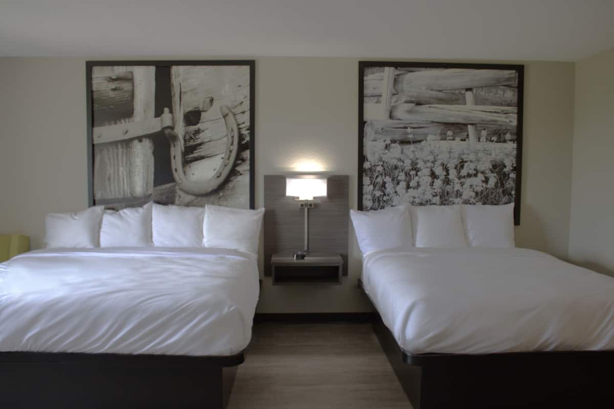 A hotel room with two beds, a nightstand with a lamp, and two large abstract paintings on the walls.