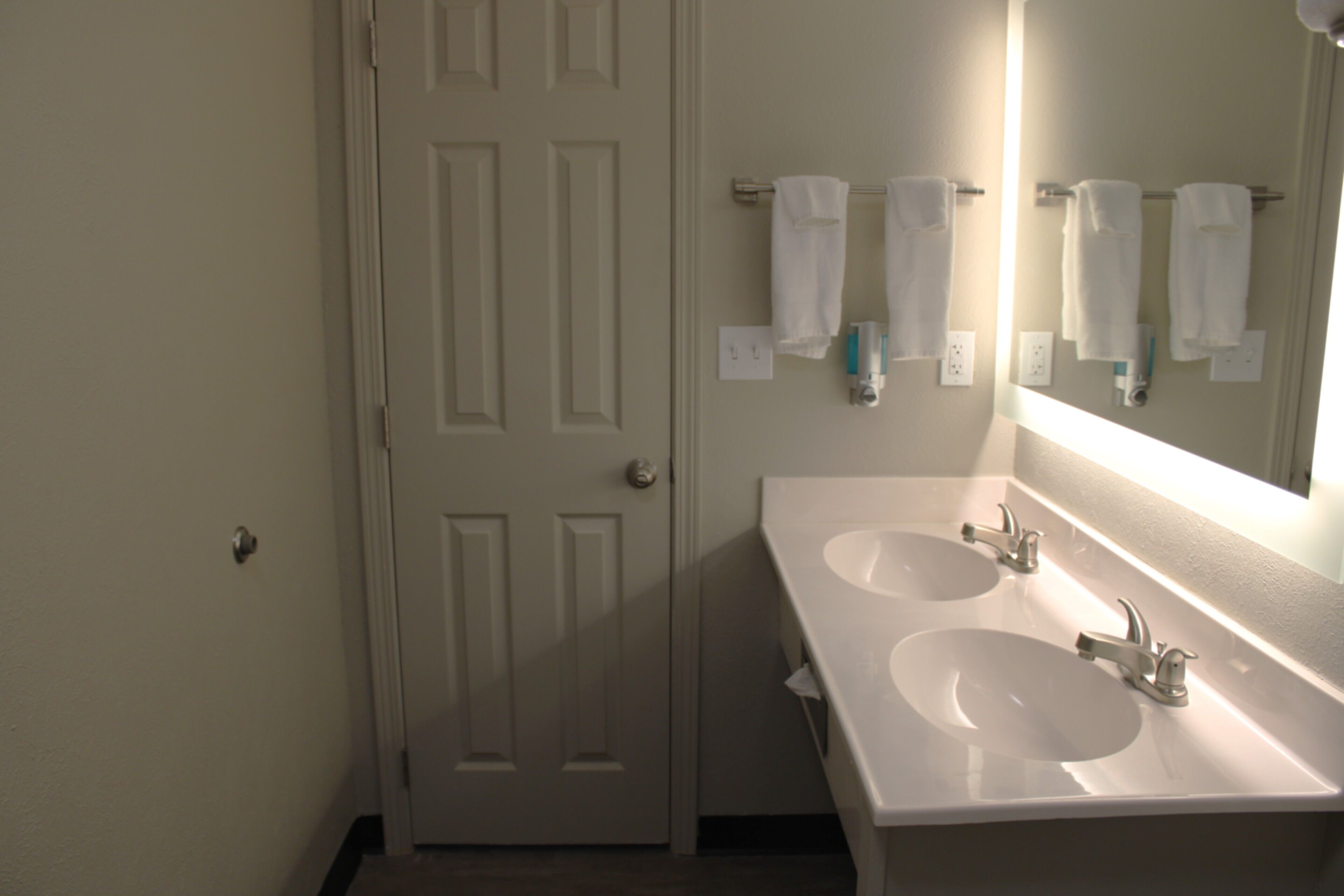 A bathroom with two sinks, a mirror, and a door.