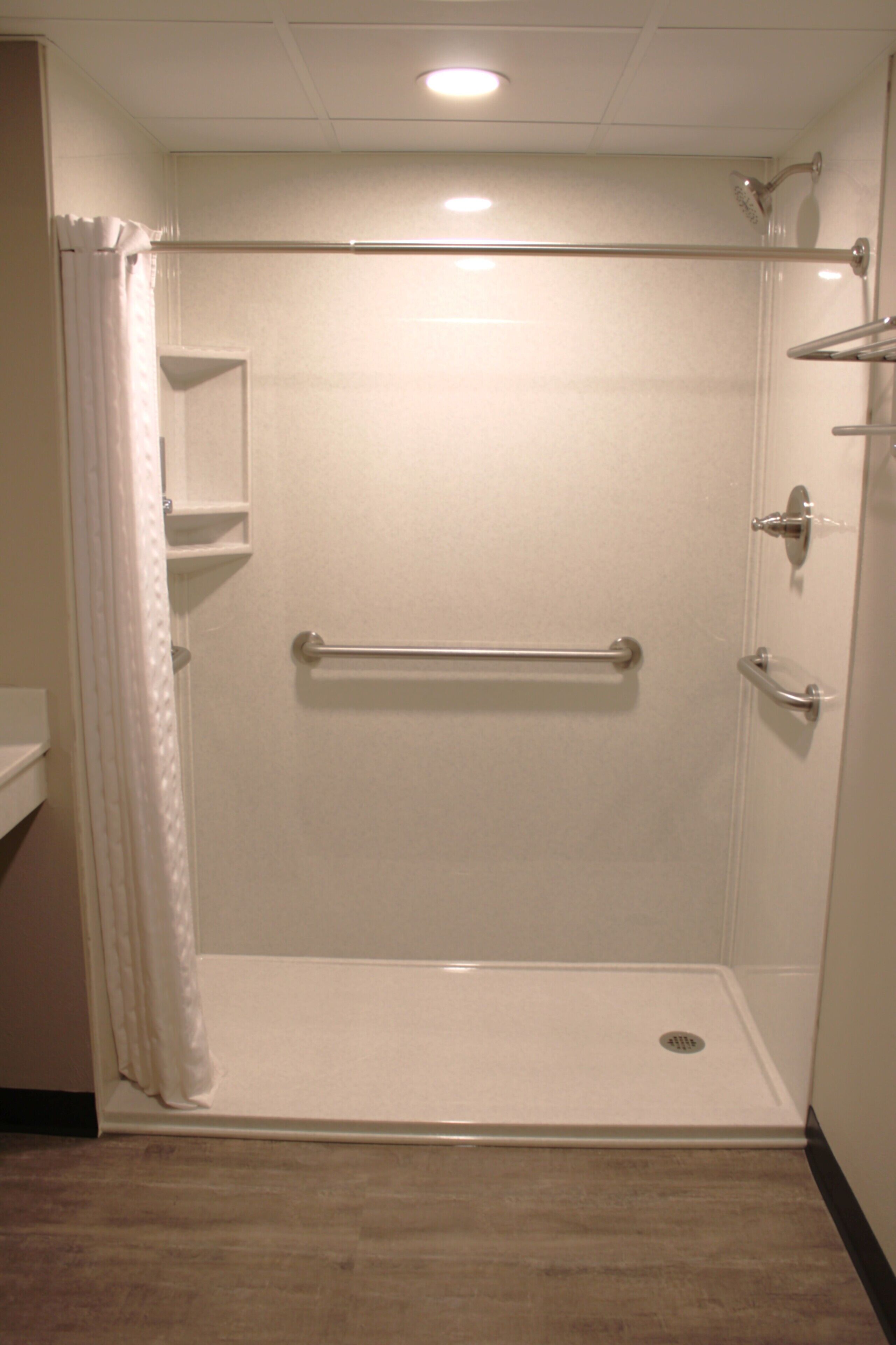 A shower with a grab bar, a shelf, and a door with a handle.