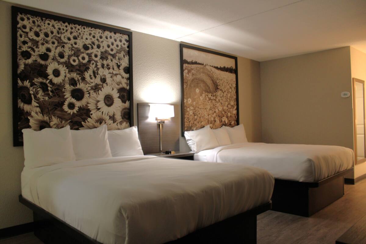 A hotel room with two beds, a large floral artwork on the wall, a bedside lamp, and a door.