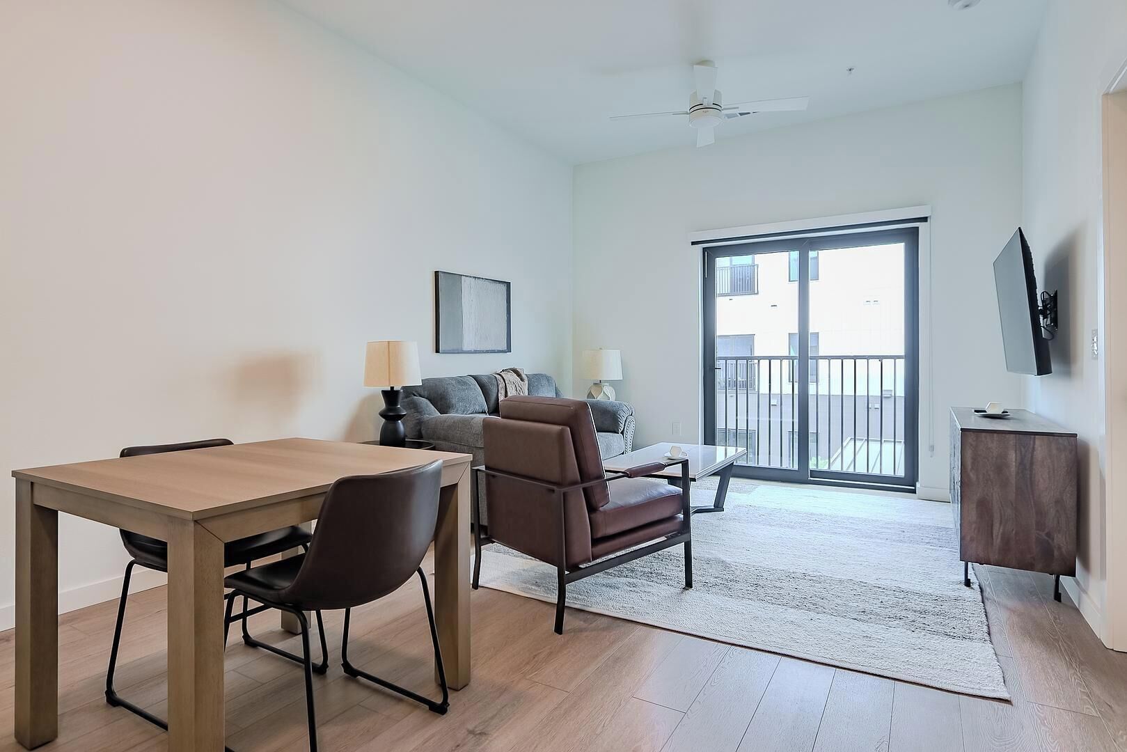 A modern living room with a dining table, two chairs, a sofa, a TV, and a balcony.