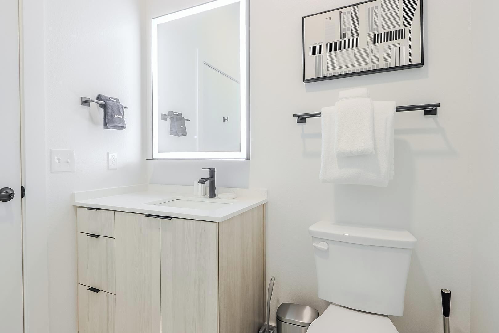 A modern bathroom with a white sink, a mirror, a toilet, and a towel rack.