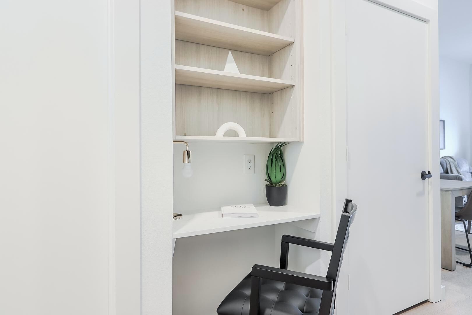 A white room with a desk, chair, and a potted plant on a shelf.