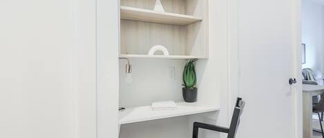 A white room with a desk, chair, and a potted plant on a shelf.