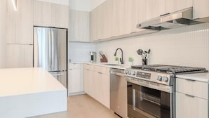 Una cocina moderna con armarios de madera clara, un refrigerador de acero inoxidable, una estufa a gas y un horno empotrado.