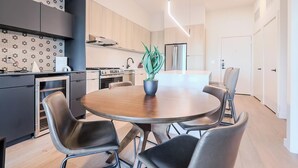 A modern kitchen with a dining area, featuring a round table with chairs, a potted plant, and a built-in oven. - Landing | Stylish 1BD, Gym, Courtyard (Houston)