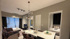 Quarto de hotel moderno com sofá, mesa de jantar, televisão e cama.