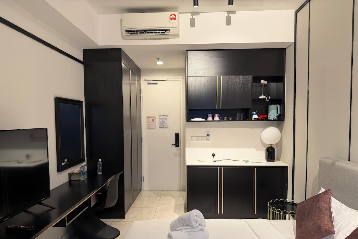 Ein modernes Hotelzimmer mit Flachbildfernseher, Schreibtisch, einem Bett mit Kissen, einem Badezimmer mit Waschbecken und Spiegel sowie einem Kleiderschrank.