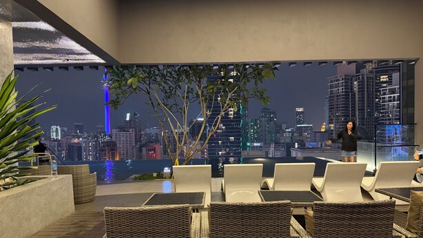 Una terrazza panoramica con poltrone in vimini, vista sulla città illuminata di notte e una persona che parla.
