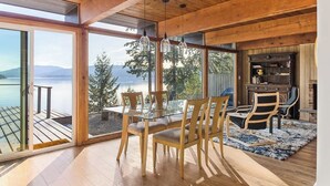 A spacious room with a wooden ceiling, a glass table with chairs, and a view of a lake.