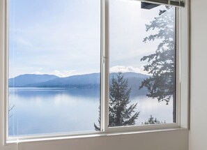 Una ventana con vista a un lago tranquilo, montañas y árboles.