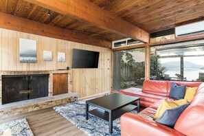 Una sala de estar moderna con chimenea, sofá de cuero y grandes ventanales con vista al agua.