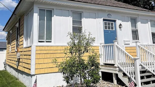 Et toetagers hus med en blå dør, hvid facade og en lille forhave med et amerikansk flag.