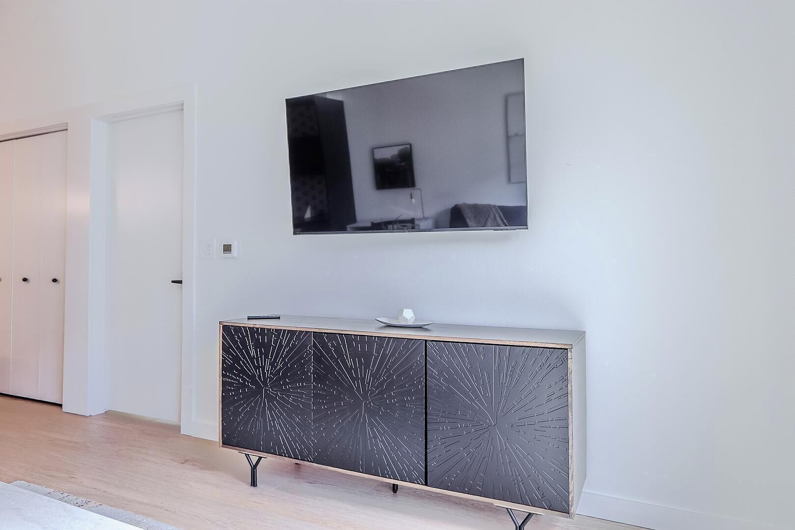Een gang met een witte deur, een zwart-wit kast en een wandgemonteerde flatscreen-tv.