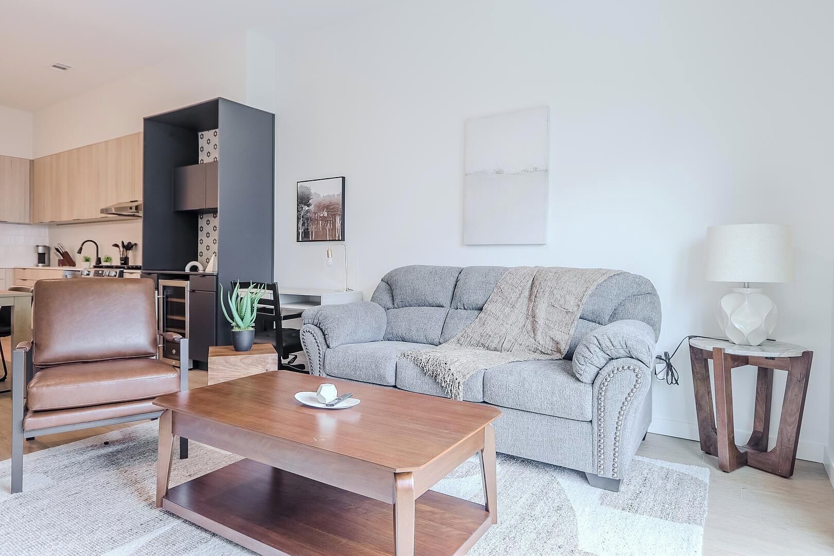 Un salon moderne avec un canapé, une table basse, un coin repas et une cuisine en arrière-plan.