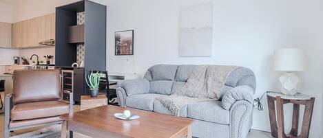 Un salon moderne avec un canapé, une table basse, un coin repas et une cuisine en arrière-plan.