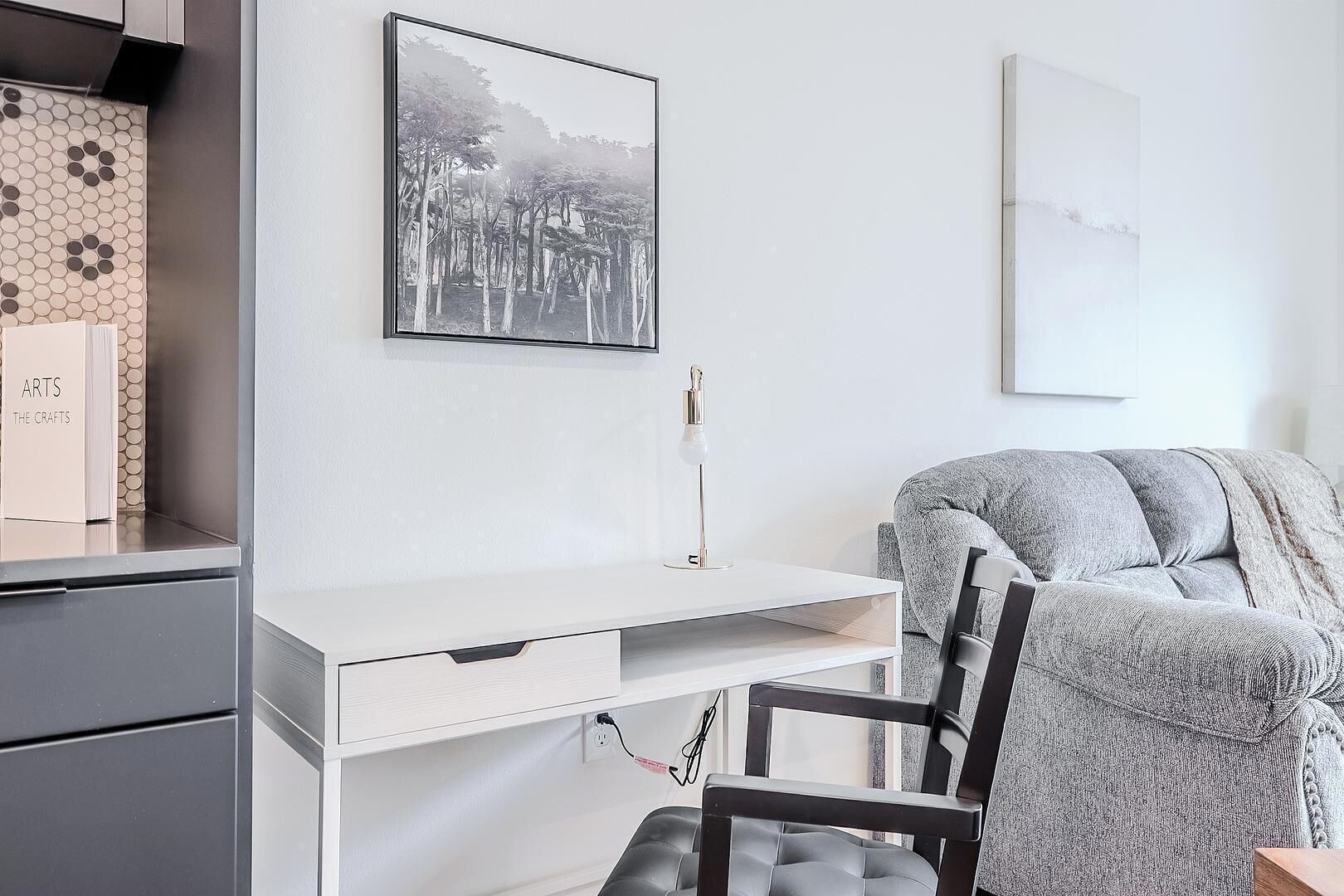 Una habitación moderna con un escritorio blanco, una silla, un cuadro enmarcado y una estantería.