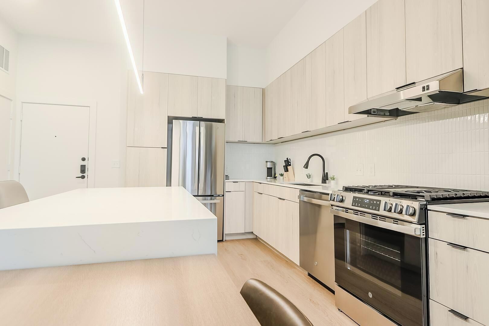 A modern kitchen with a central island, stainless steel appliances, and light wood cabinetry.