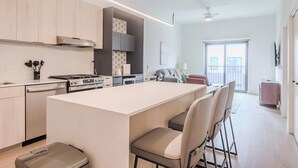 A modern kitchen with a central island, a dining area with chairs, and a view to the outside. - Landing | Modern 1BD, Gym, Courtyard (Houston)