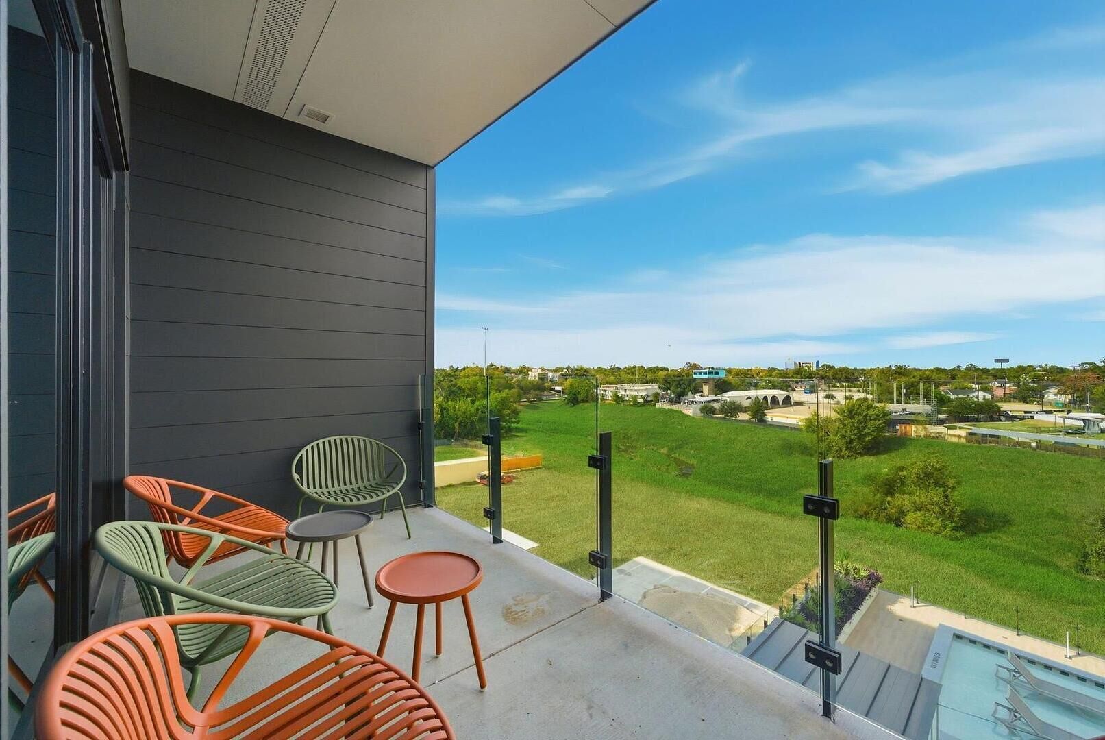 A balcony with outdoor furniture, a pool, and a view of a green landscape and buildings.