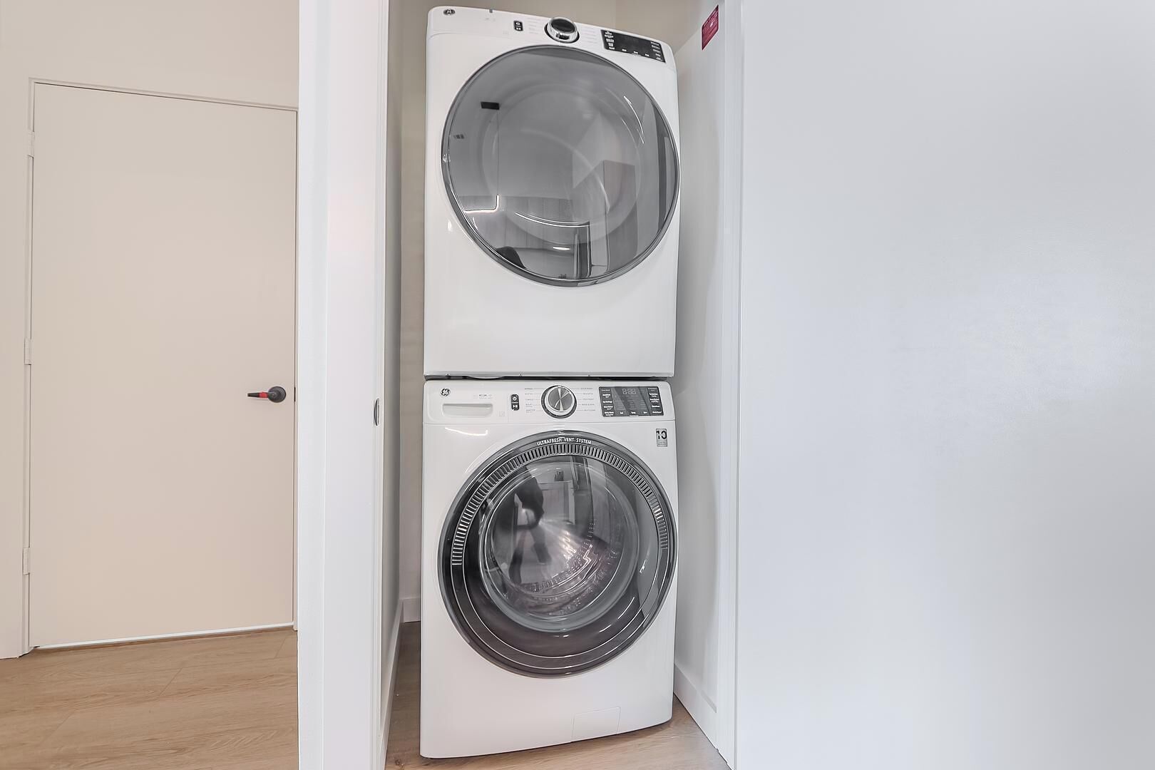 Un appareil compact, blanc, combinant lave-linge et sèche-linge, fixé au mur dans un couloir.