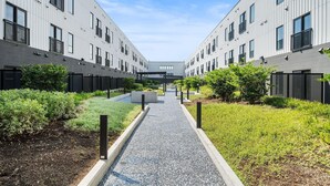 A modern building with a central pathway flanked by greenery and a clear sky. - Landing | Stunning 1BD, Gym, Courtyard (Houston)