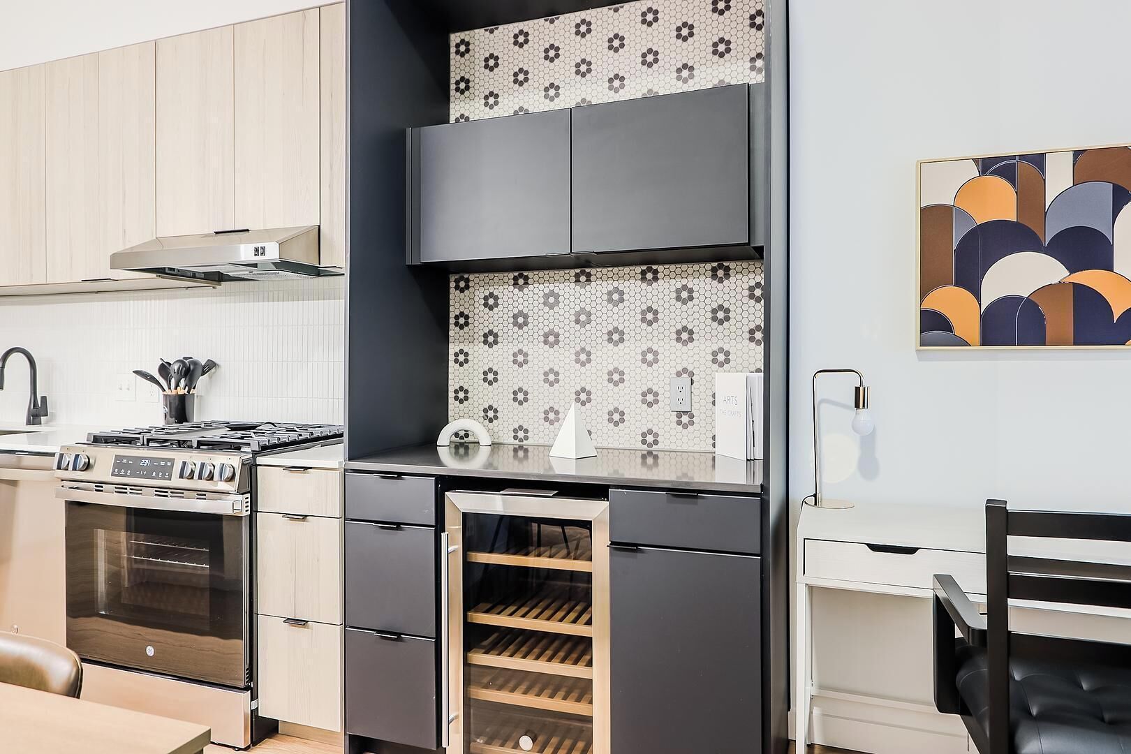 Een moderne keuken met een inbouwoven, een kookplaat, een wijnkoeler en een eethoek met een stoel.