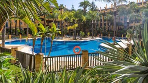 Une piscine entourée de palmiers et un bâtiment doté de balcons.