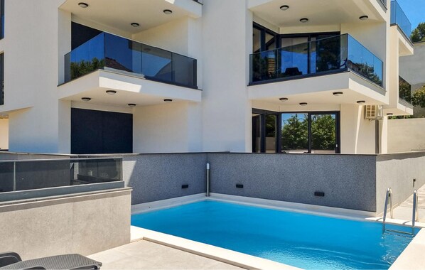 Un immeuble moderne à plusieurs étages, doté d’une piscine, de balcons et offrant une vue sur un ciel dégagé.