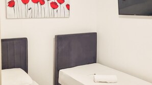 To enkeltsenge med grå sengegærder og hvide sengetæer, et fladskærms-tv monteret på væggen, og et billede af røde blomster over sengene.