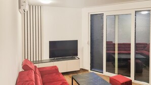 En stue med fladskærms-tv, rød sofa og sofabord.
