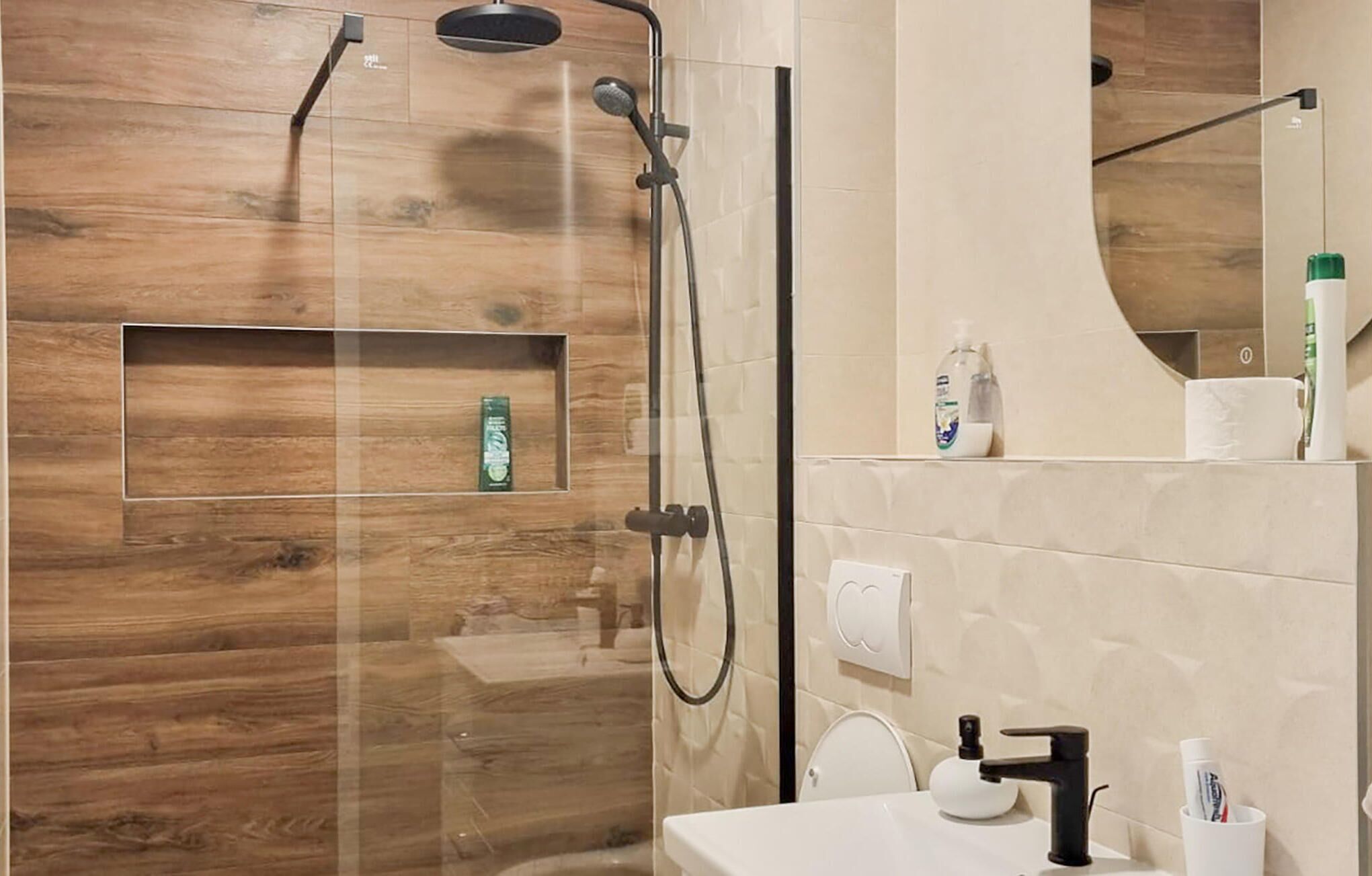 A modern bathroom with a wooden wall, a glass-enclosed shower, and a sink with toiletries.