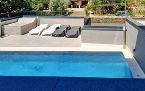 Une piscine sur le toit, dotée de chaises longues et bordée d’un mur en pierre.