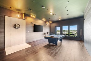 A modern room with a pool table, dartboard, and large windows offering a view. - Landing | Stylish 1BD, Courtyard, Gym (Houston)