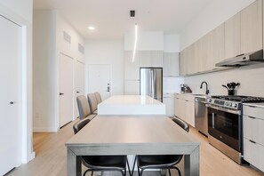 A modern kitchen with a central island, stainless steel appliances, and light wood cabinetry. - Landing | Stylish 1BD, Courtyard, Gym (Houston)