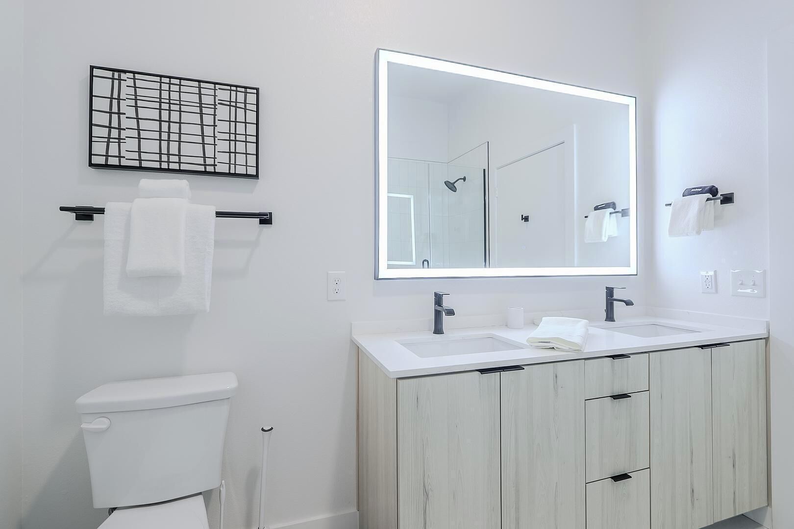 A modern bathroom with a toilet, a sink, a mirror, and a shower.
