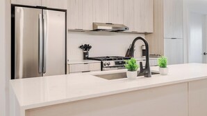 Een moderne keuken met een roestvrijstalen koelkast, een gasfornuis, een zwarte kraan en twee potplanten op het aanrecht.