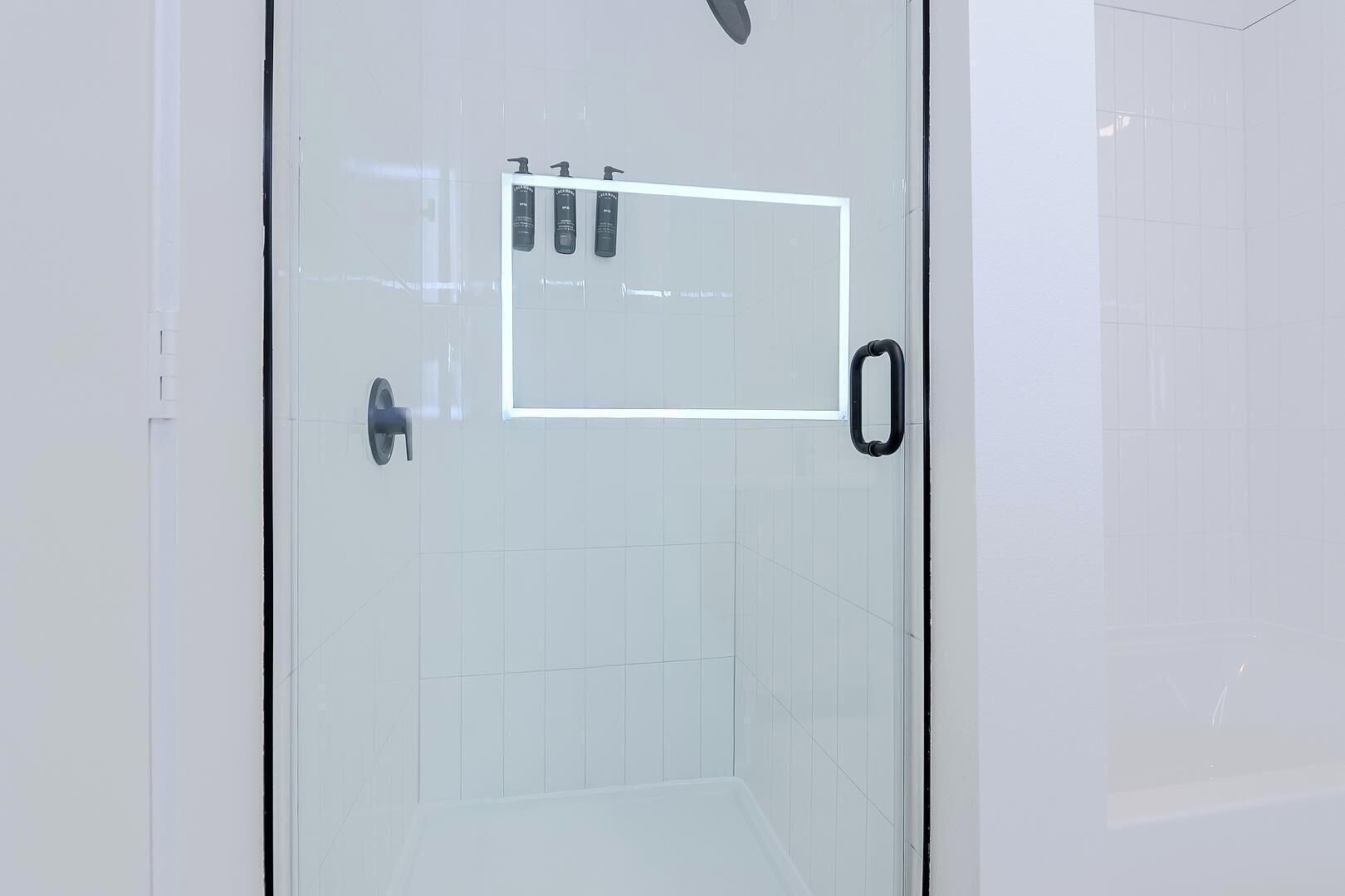 A glass door with a handle, a small shelf with toiletries, and a tiled floor.