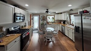 Una cocina moderna con armarios blancos, electrodomésticos de acero inoxidable, una mesa de comedor con sillas y un ventilador de techo.