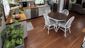 Una cocina con armarios blancos, encimera de madera, una mesa de comedor con sillas blancas y un ventilador de techo.