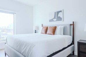 Ein modernes Hotelzimmer mit einem großen Bett, einem Nachttisch, einer Lampe und Blick auf die Stadt.