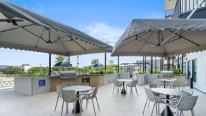 Um terraço no telhado com mesas ao ar livre, churrasqueira e guarda-sóis.